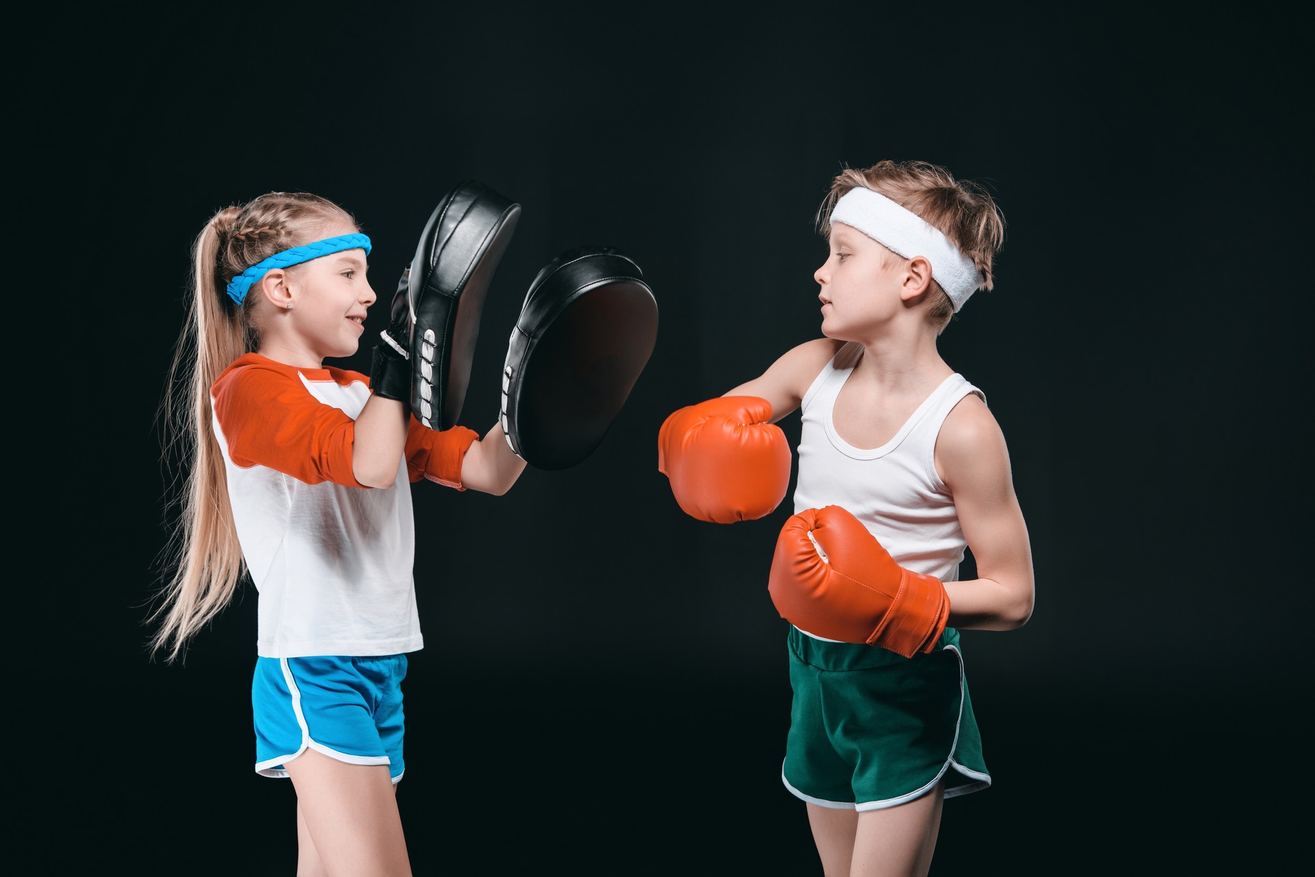 Side view of boy and girl in sportswear boxing isolated on black, activities for children concept